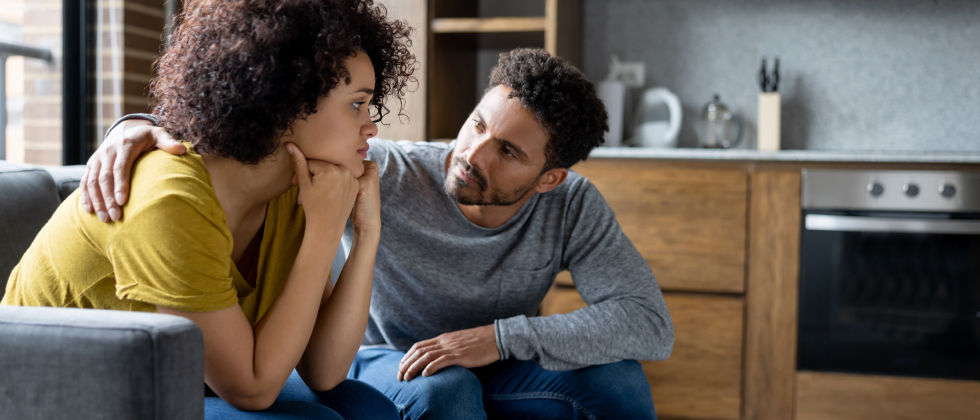 women and man sitting on a sofa, he puts his arm around her